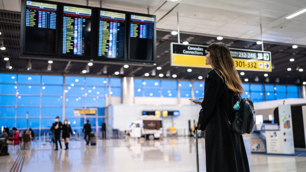 Mujer con una maleta parada en una terminal buscando su vuelo en el panel